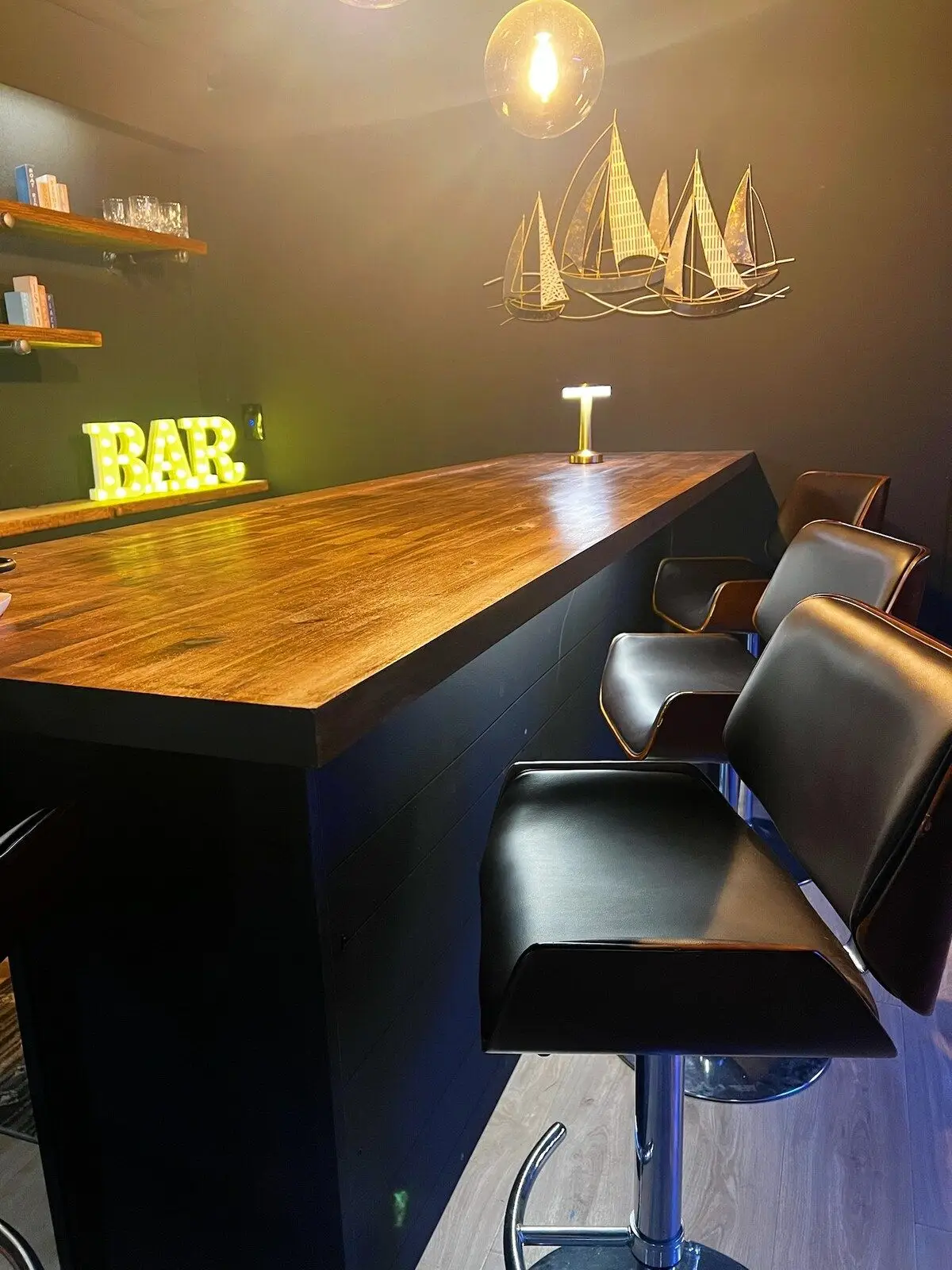 The Paddle Inn's basement bar, a live-edge wood counter with leather stools, a lit BAR sign, and sailboat wall art