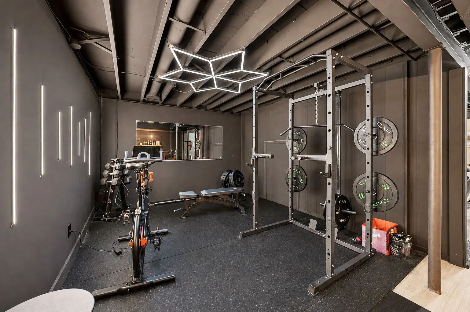 Home gym in the basement with a squat rack, weight bench, dumbbells and a spin bike