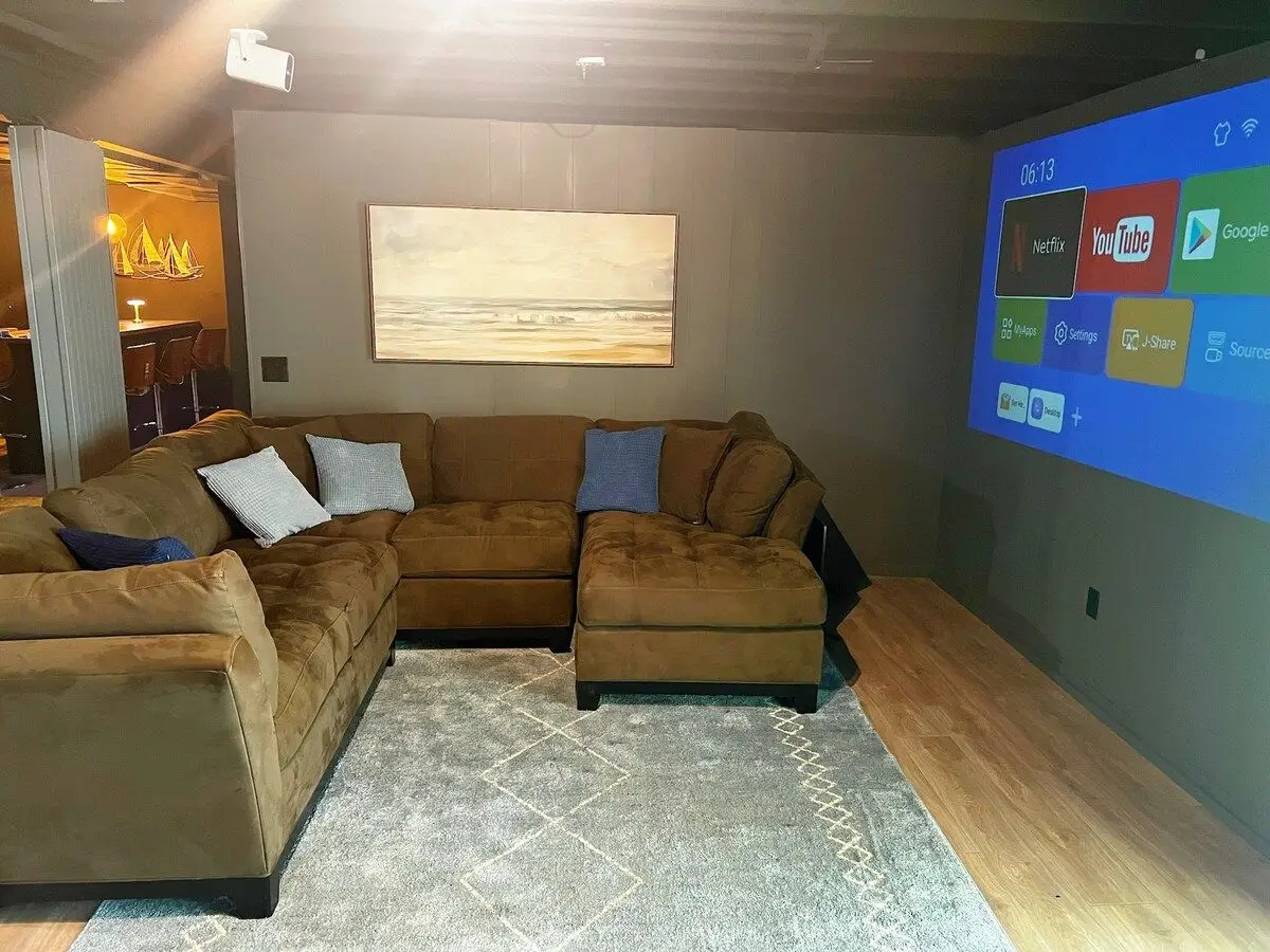 Basement lounge with a large sectional sofa facing a wall-sized projector screen