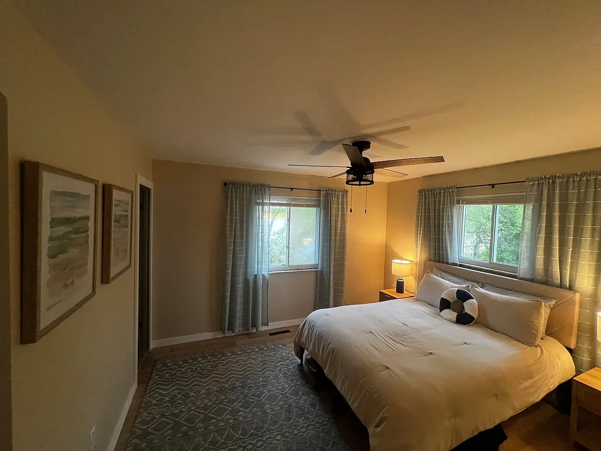 Bedroom with a king bed, ceiling fan, and windows on two walls