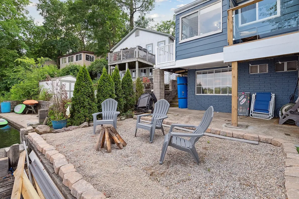 The fire pit and turf lawn with the blue two-storey lake house rising behind