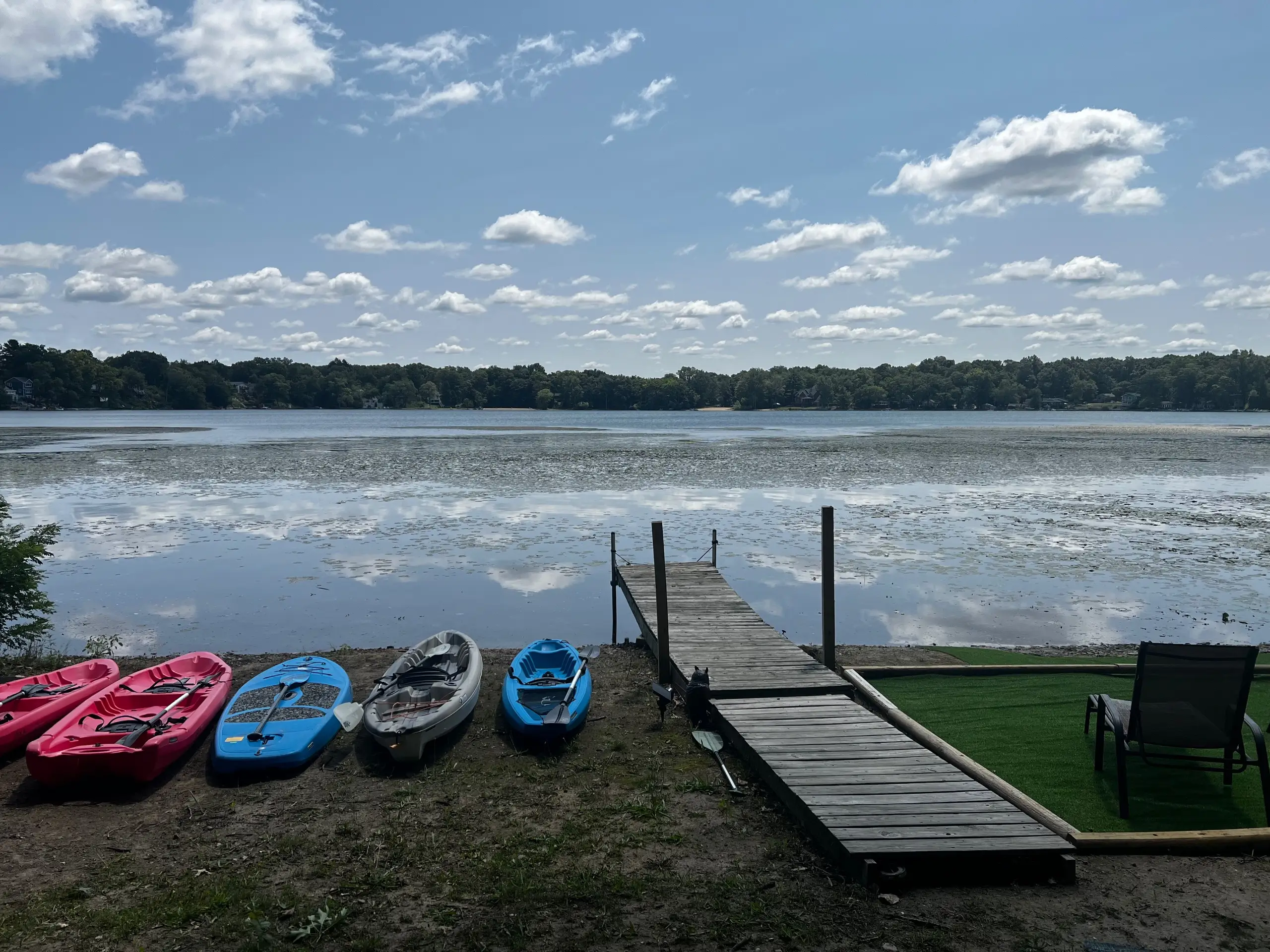 Kayaks and a stand-up paddleboard pulled up on the shoreline beside the Paddle Inn's wooden dock, looking across Briggs Lake on a clear day