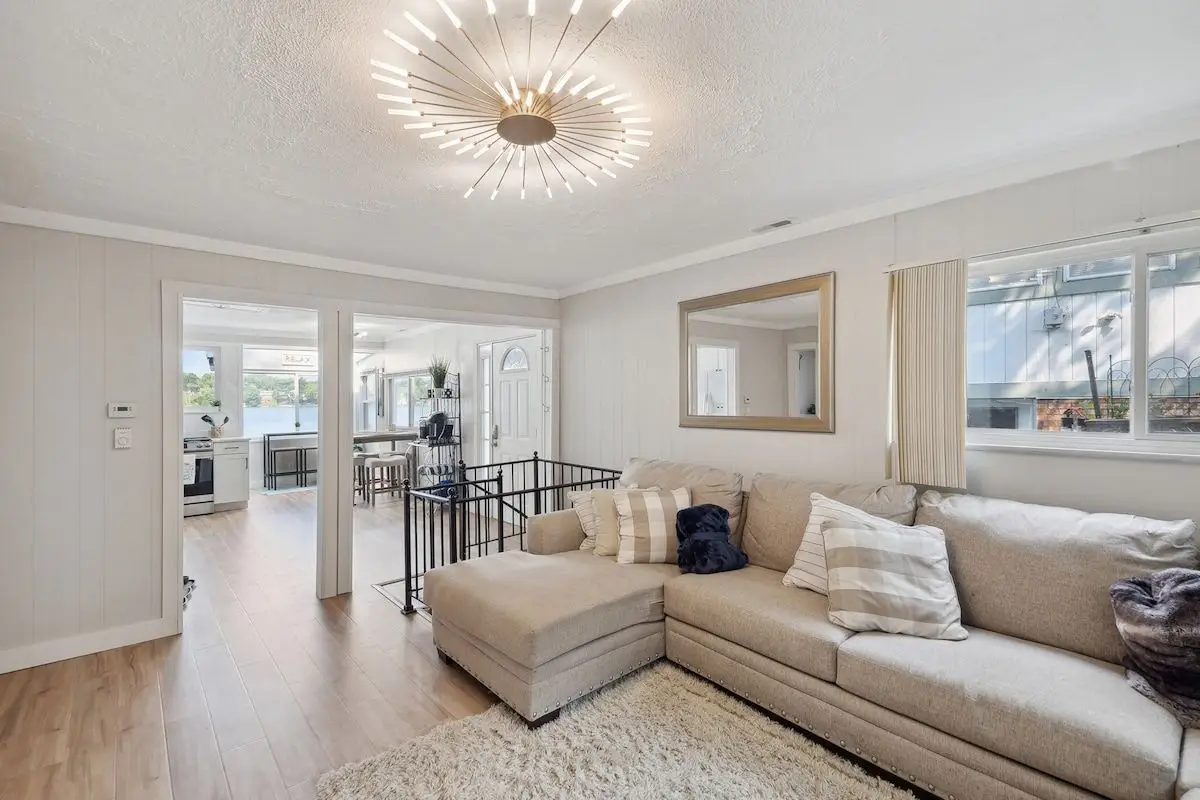 Bright living room with a sectional sofa, a starburst light fixture, and a view through to the kitchen and lake