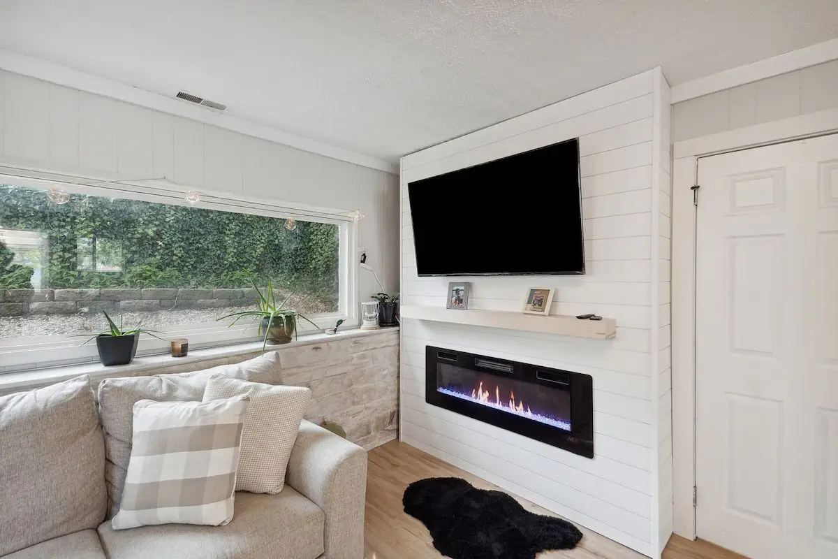 Sitting area with a wall-mounted television above a linear electric fireplace and a window seat