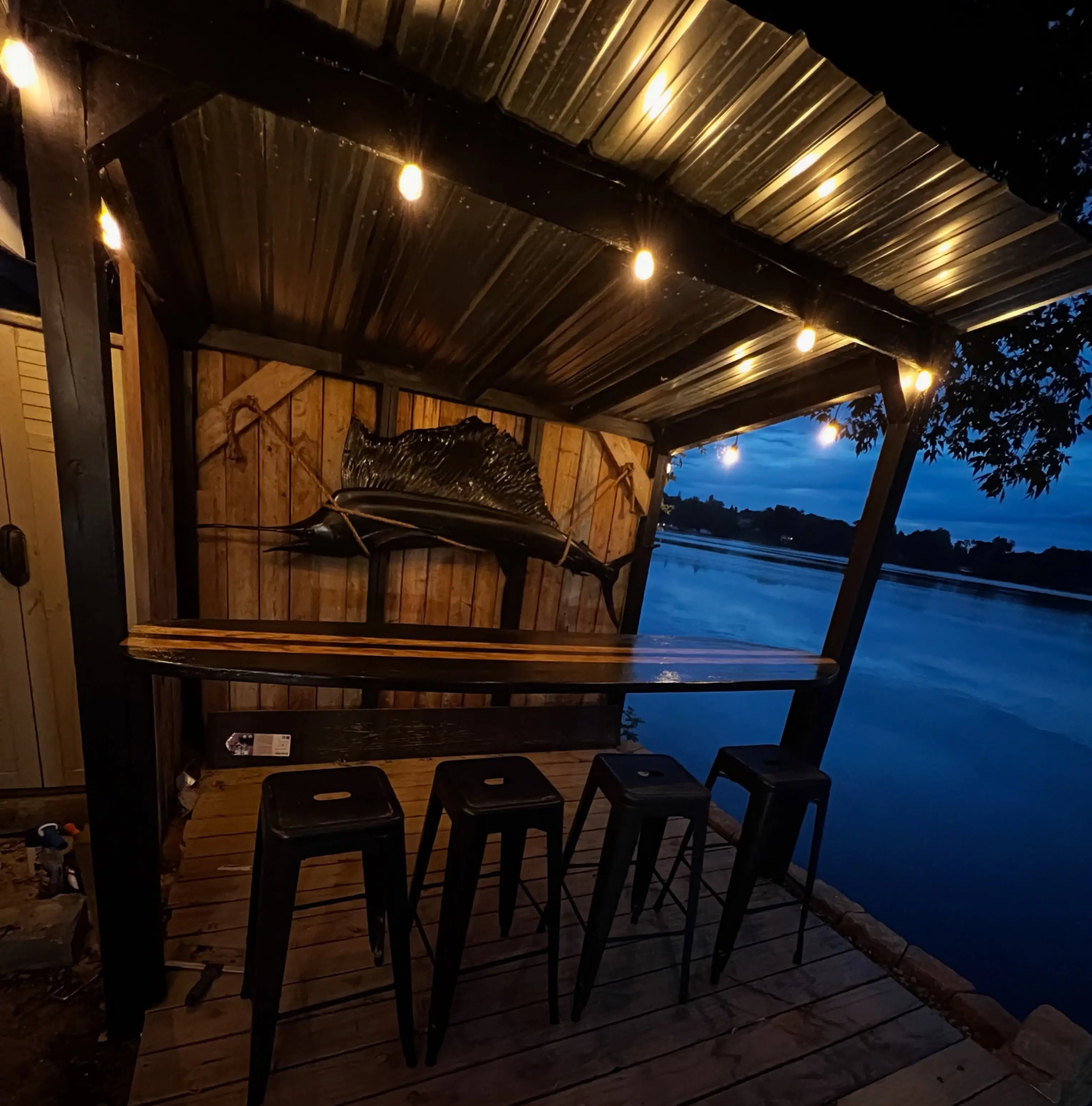 The tiki bar at dusk, lit by string lights, with the mounted marlin above the counter